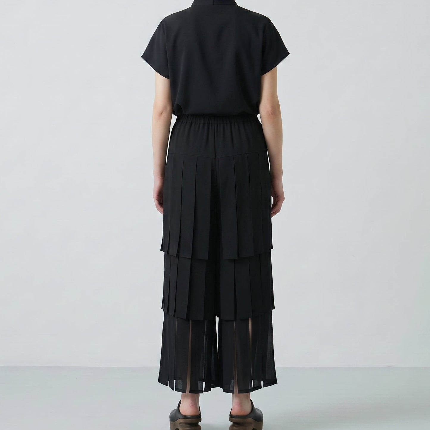 Person wearing a black outfit with layered skirt on a white background
